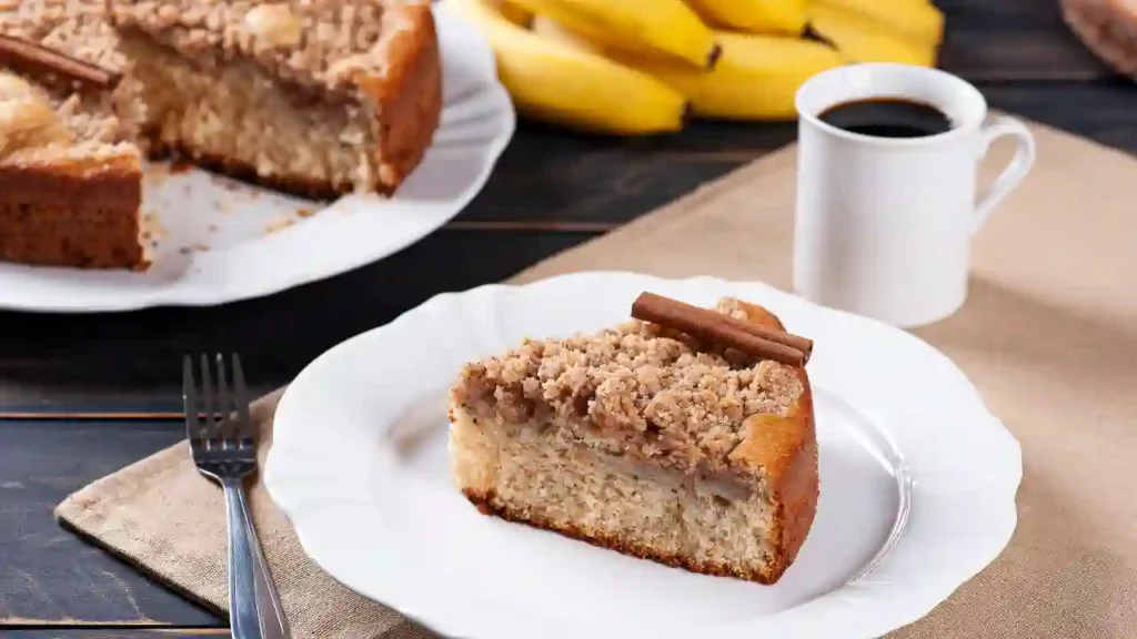 Fatia de coffee cake com farofa crocante e canela, servida com café e bananas — inspirada nas receitas da Ana Maria Braga.