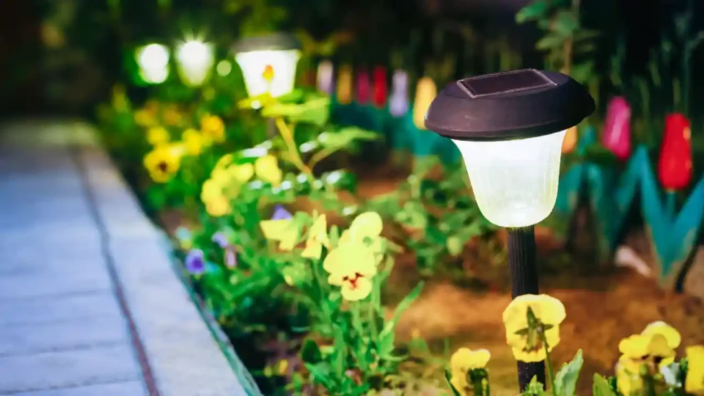 Caminho de jardim iluminado por luzes solares entre flores coloridas, revelando o segredo da iluminação no quintal.