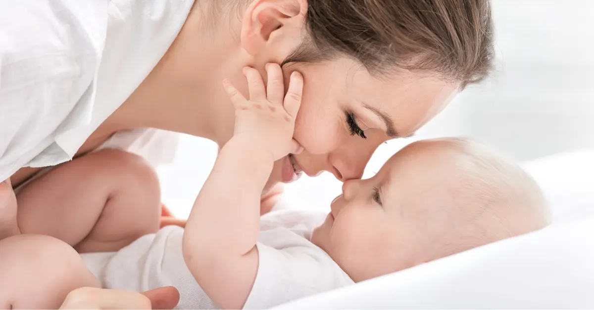 Mãe tocando carinhosamente o rosto do bebê, demonstrando o vínculo nos primeiros meses de vida.