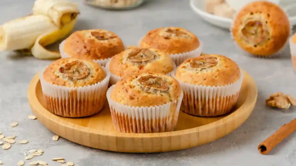 Bolo de banana com aveia sem açúcar servido em um prato claro, com fatia cortada à frente e bananas caramelizadas por cima, decorado com flocos de aveia.